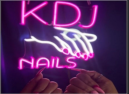 Custom pink and white neon sign for “KDJ Nails” featuring a stylized hand and nails graphic, held in front of the sign by a customer.