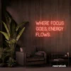 Where Focus Goes Energy Flows neon sign in peachy pink for productivity decor and creative inspiration.